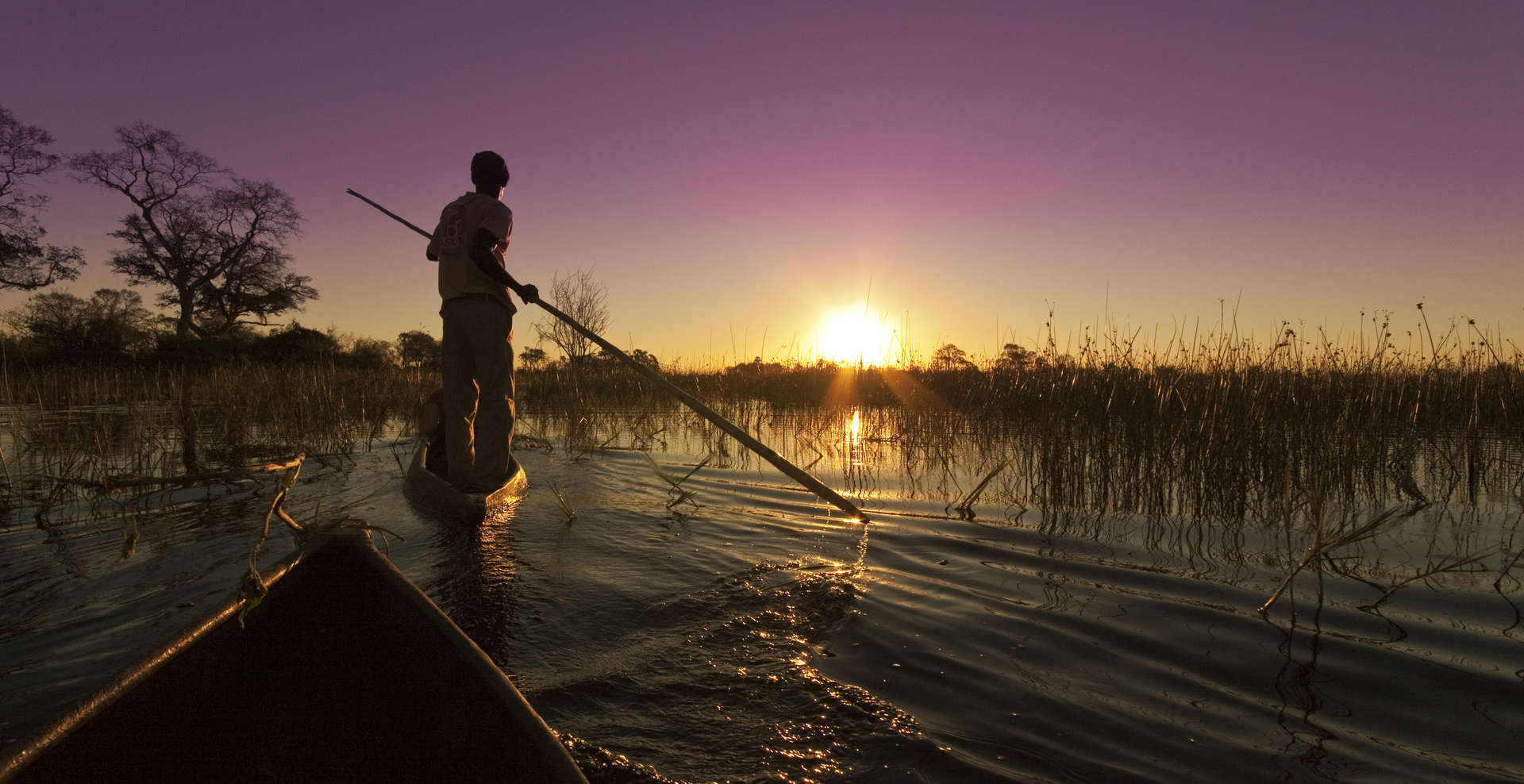 The sun setting over the Okavango Delta from the view of a traditional mokoro (canoe)