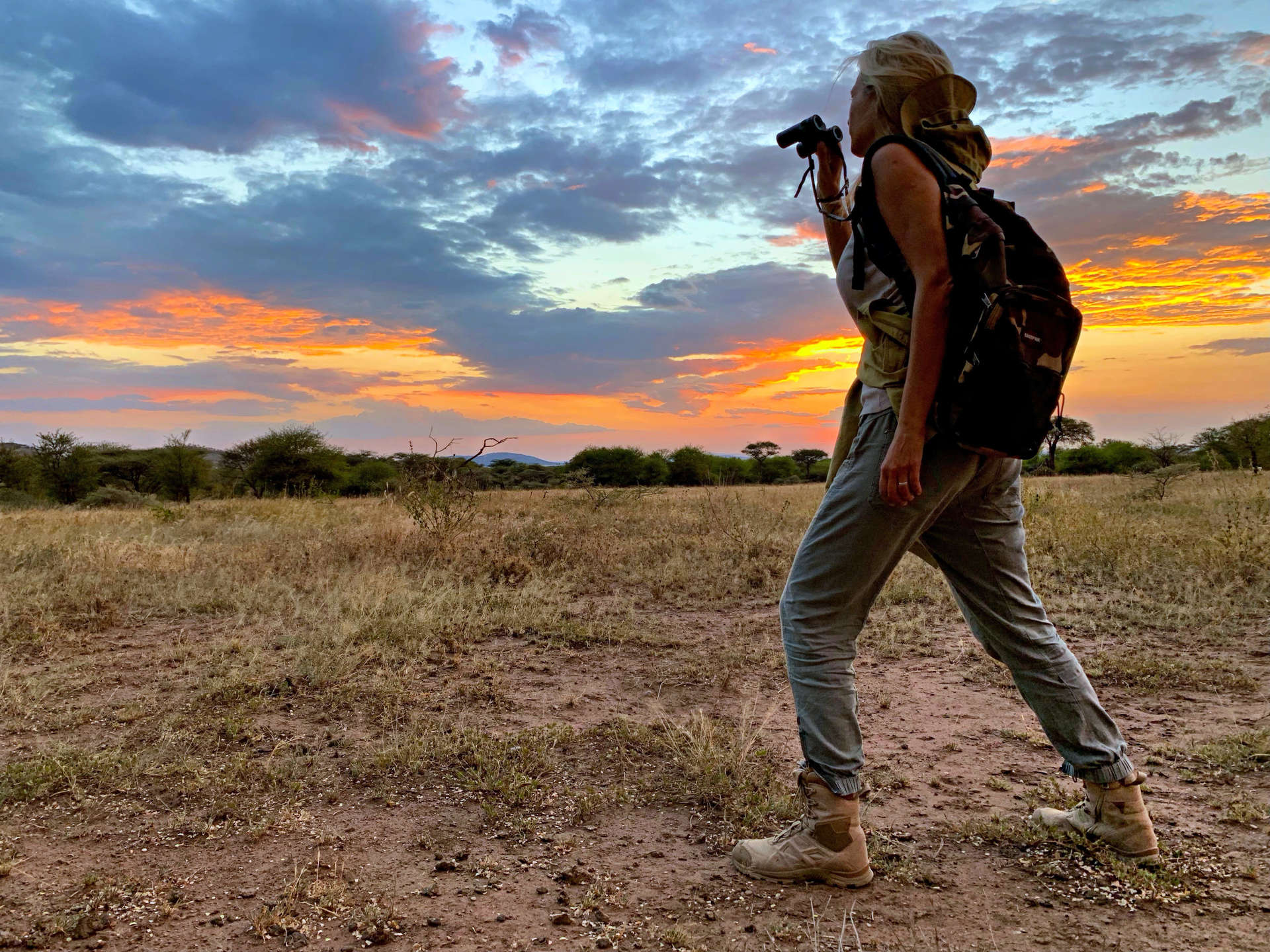 Woman Photographing While Walking On Field Against Sky During Sunset